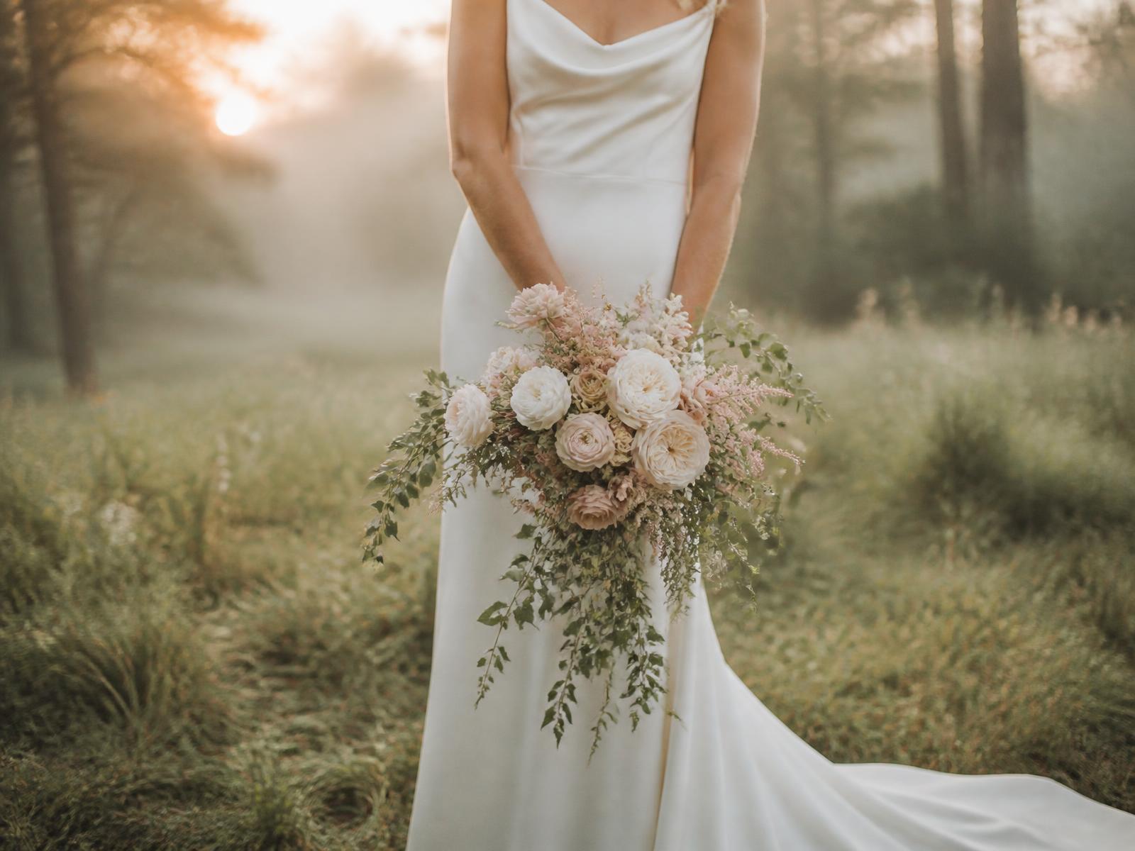 Bride holding a garden-style bouquet of ivory and blush blooms in a misty Pennsylvania meadow at golden hour